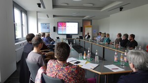 Menschen sitzen an Tischen und verfolgen eine  Präsentation