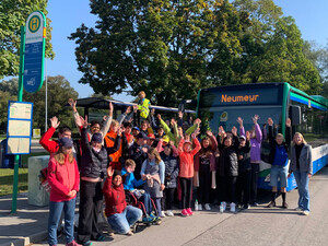 25 Jugendliche stehen vor zwei Linienbussen und winken.