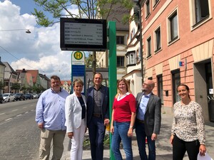 Sechs Personen stehen vor digitaler Busanzeige.