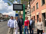 Sechs Personen stehen vor digitaler Busanzeige.
