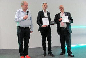Drei Männer, Personen mitte und rechts halten Urkunde.