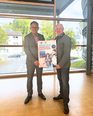 Thomas Karmasin und Guido Amendt halten Plakat "Ein Tag Azubi" in dieKamera.
