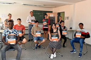 Foto:Zeigt 6 Schüler der Berufsintegrationsklasse Fürstenfeldbruck im Klassenzimmer. Dahinter stehen 2 Lehrkräfte, Landrat Karmasin und die Bildungskoordinatorin. Alle halten Bildungspässe in der Hand.
