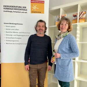 Mann und Frau stehen vor Plakat der Verbraucherzentrale