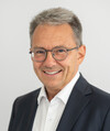 Porträtfoto eines Mannes mit Brille im schwarzen Anzug ohne Krawatteg