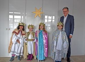 Vier kostümierte Kinder, eines hält einen Stab mit Stern an der Spitze, und ein Mann.