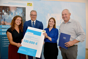 Zwei Frauen und zwei Männer halten ein Plakat mit der groß gedruckten Zahl 130.000 in die Kamera.